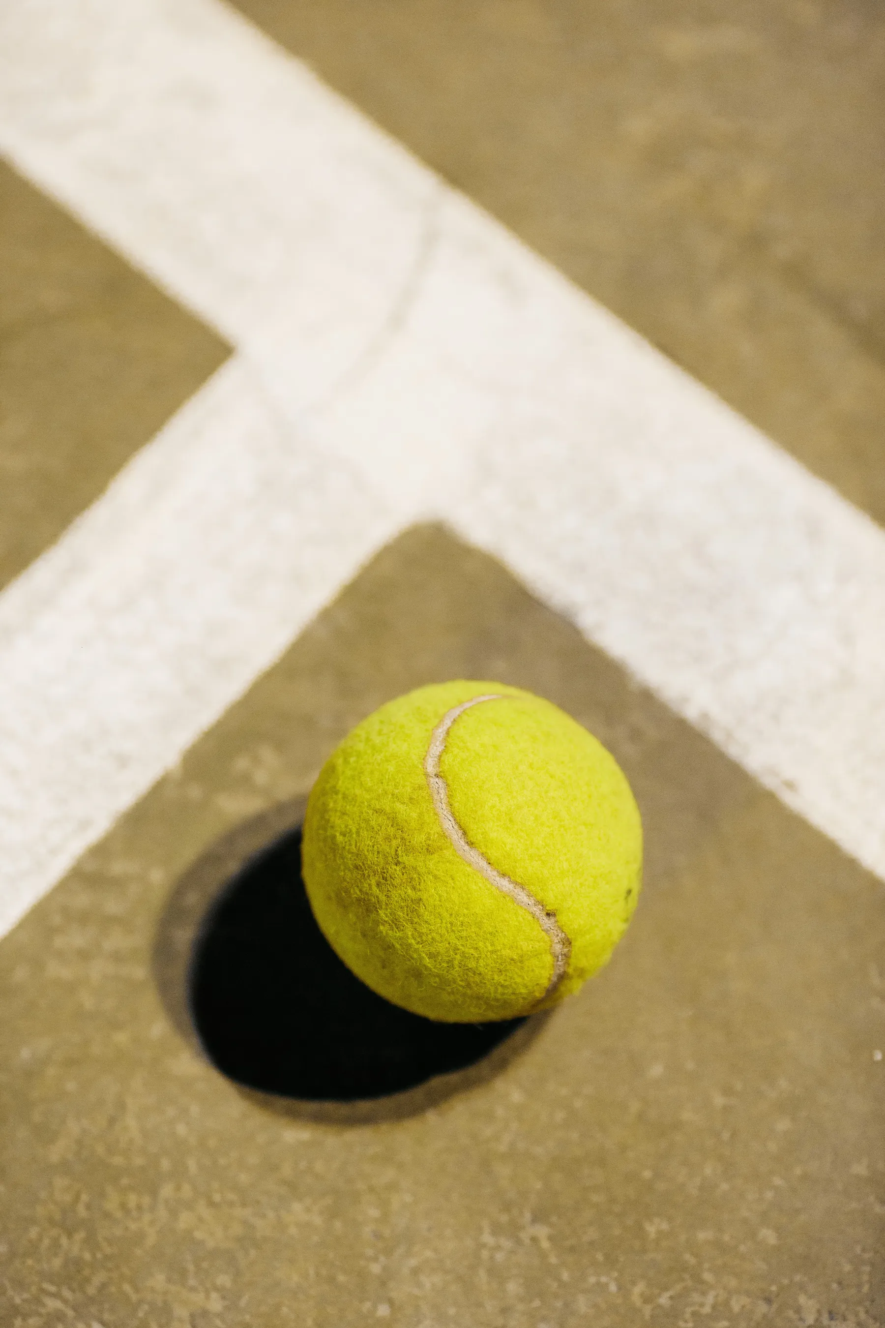 A well-used tennis ball resting where two painted court lines meet