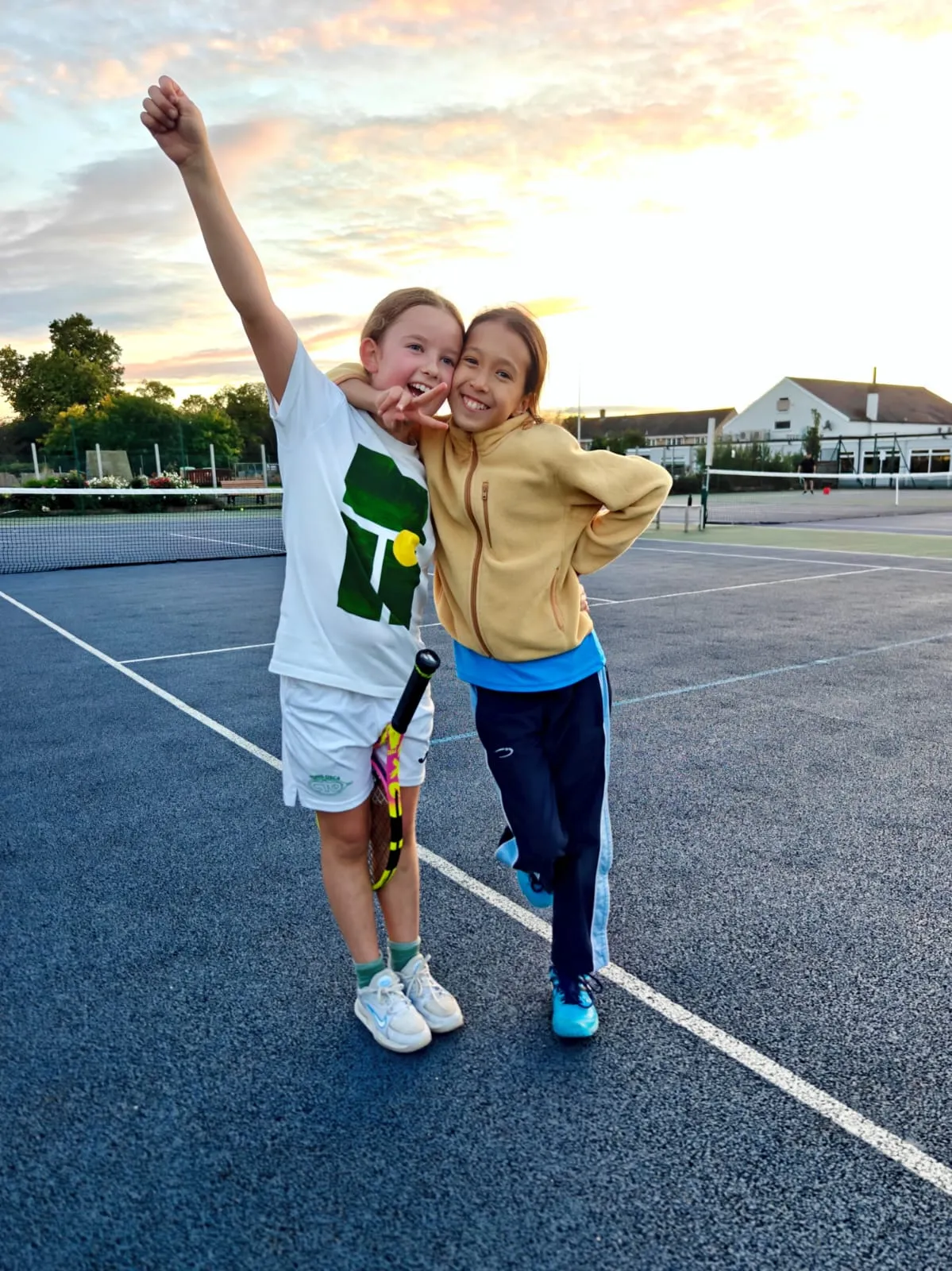 Two young players with their arms round each other, celebrating on court at sunset
